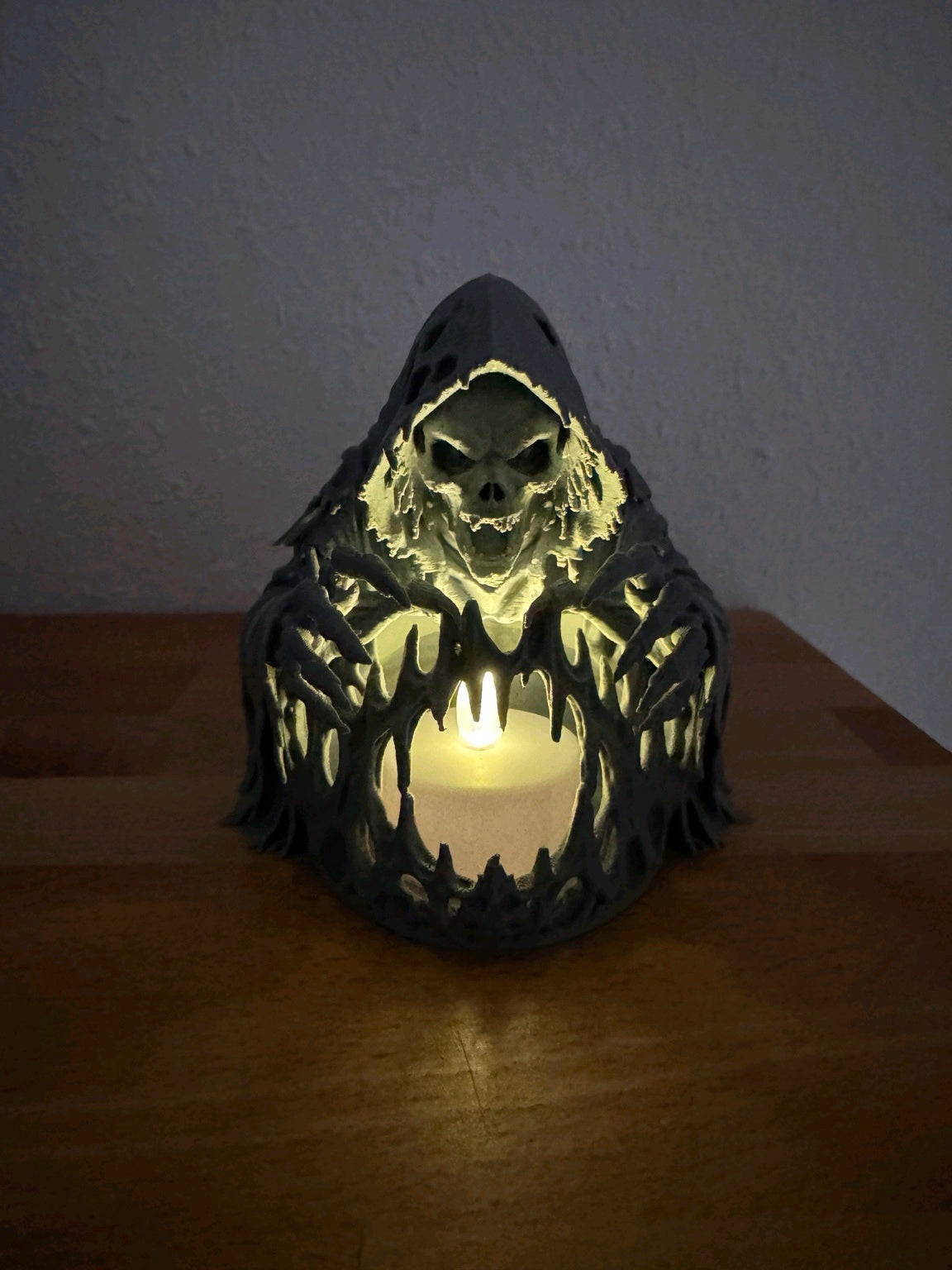 Second view of the black hooded skeleton tealight holder with its LED light on a dark wooden table