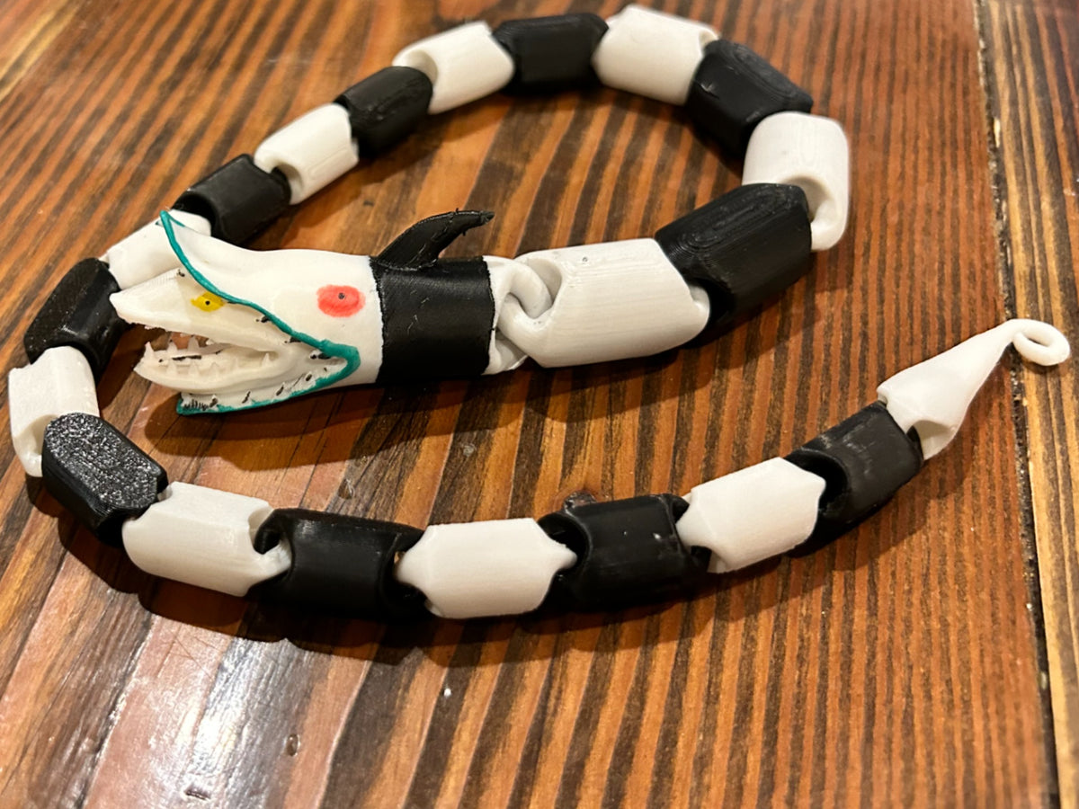 Black and white articulated snake fidget toy coiled on a wooden table