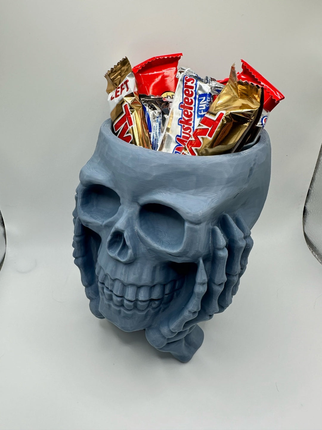 Grey skull sweet bowl held in sculpted skeletal hands, filled with wrapped sweets