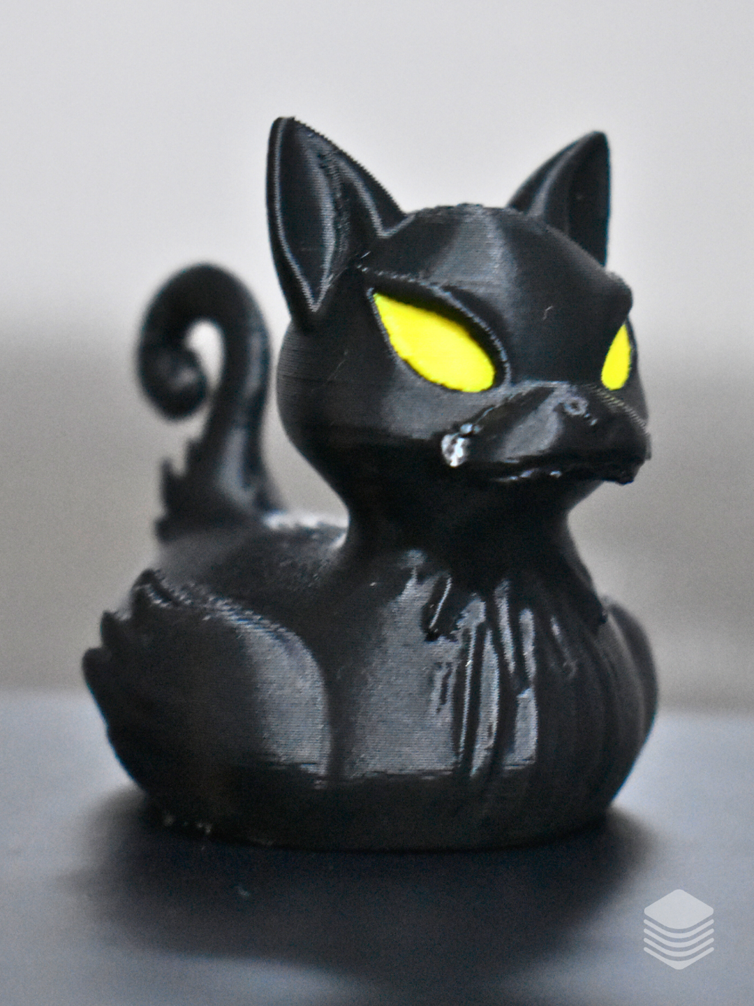 Glossy black cat bath duck with vivid yellow eyes, pointed ears and curled tail
