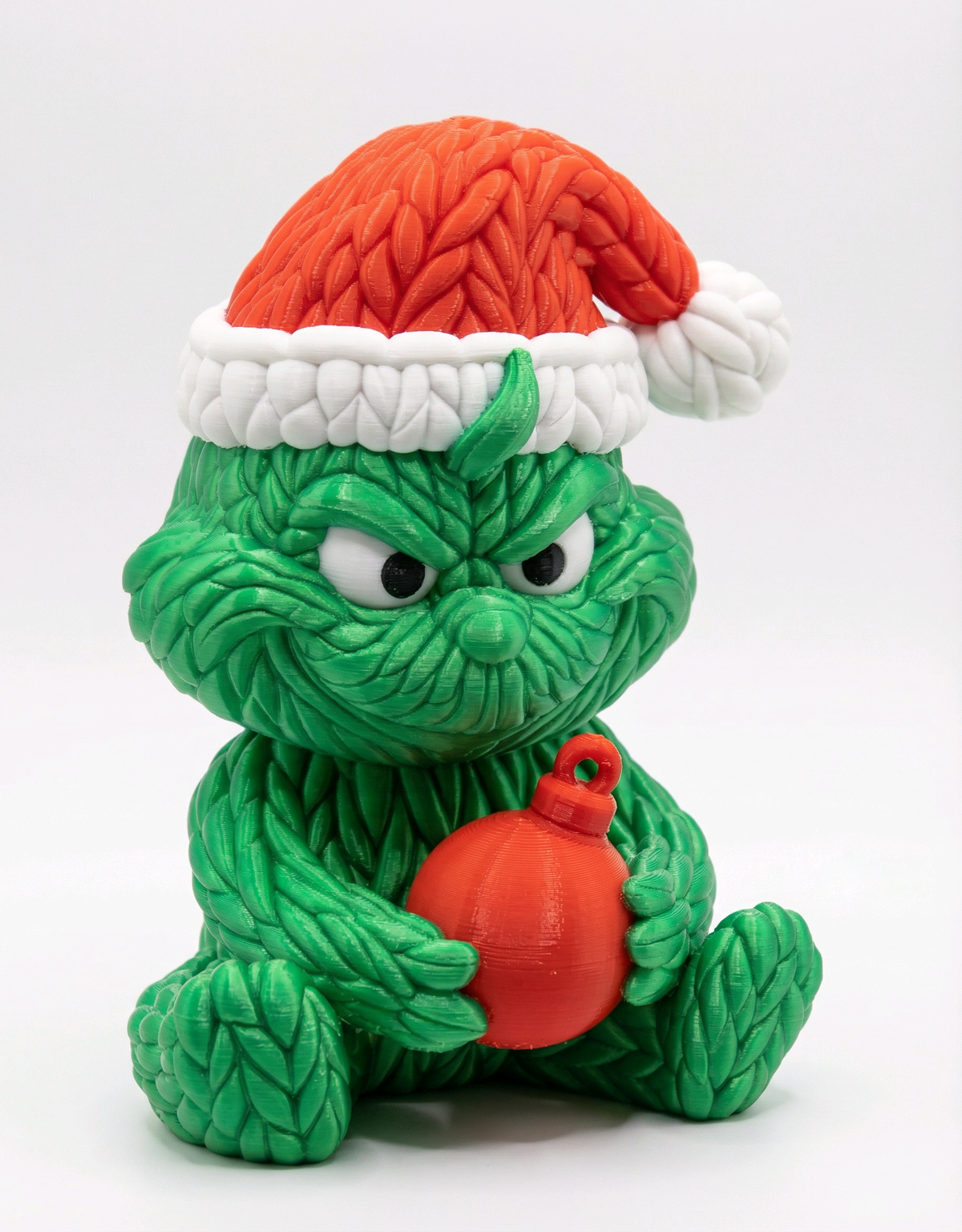 Seated green knitted-look Christmas figure wearing a red Santa hat and holding a red bauble