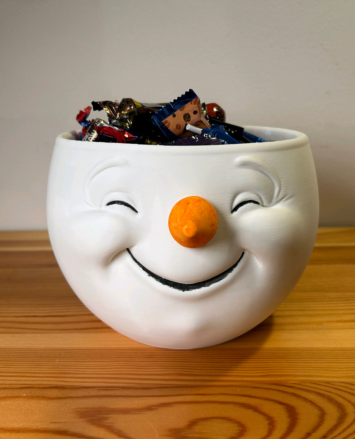 White snowman-head snack bowl with an orange nose filled with wrapped sweets