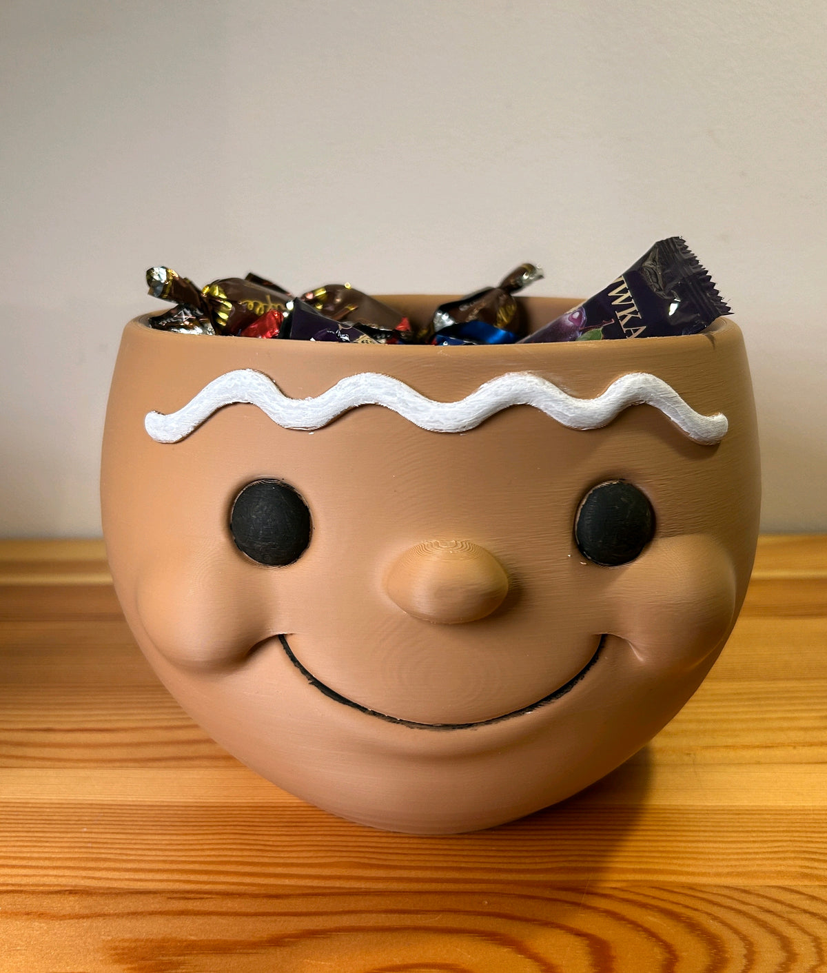 Brown snowman-head snack bowl with white wavy trim filled with wrapped sweets
