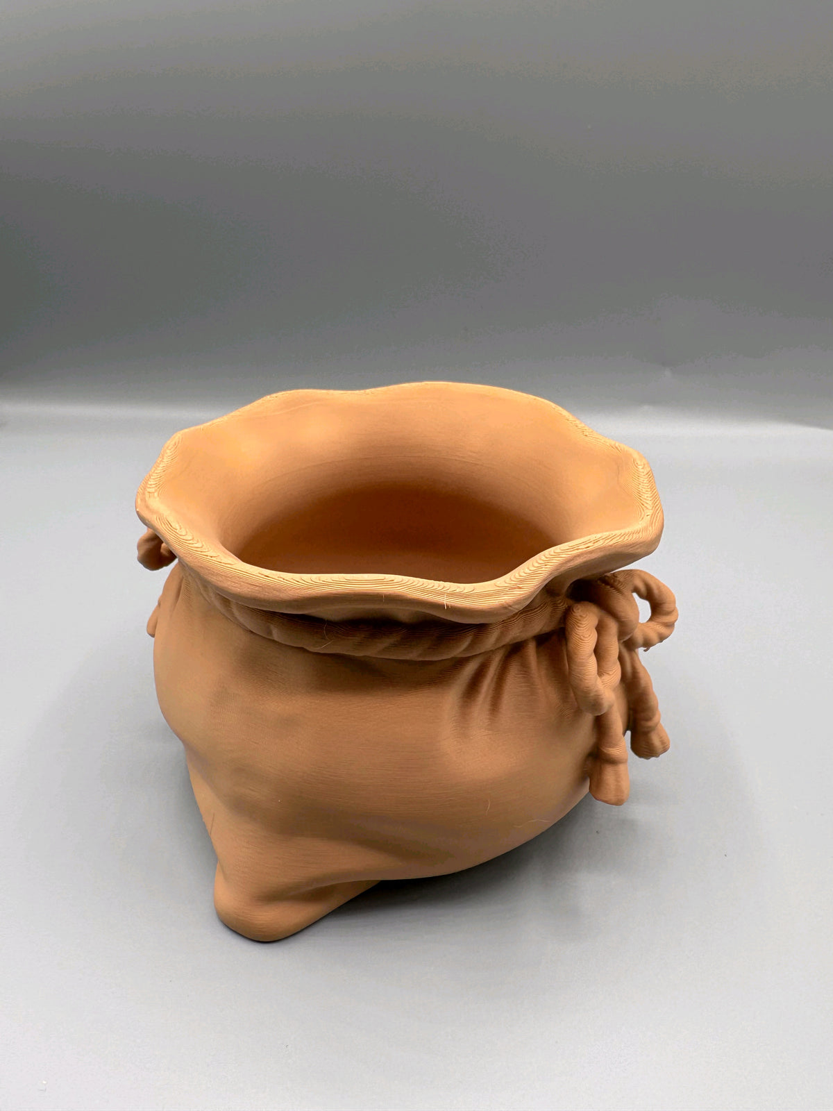 Front view of tan sack-shaped sweet bowl with braided rim and decorative rope bow