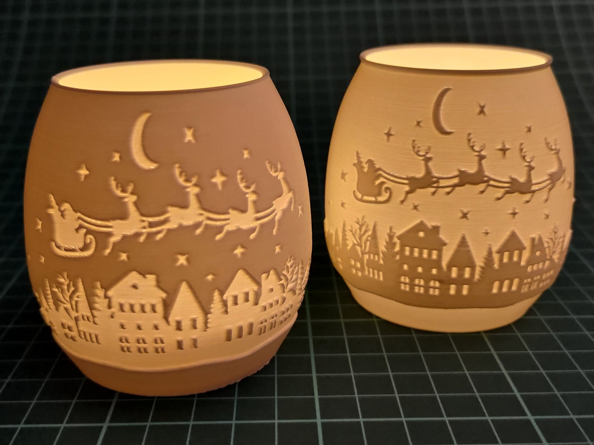 Two amber Christmas village tealight holders with a glowing Santa sleigh and reindeer scene