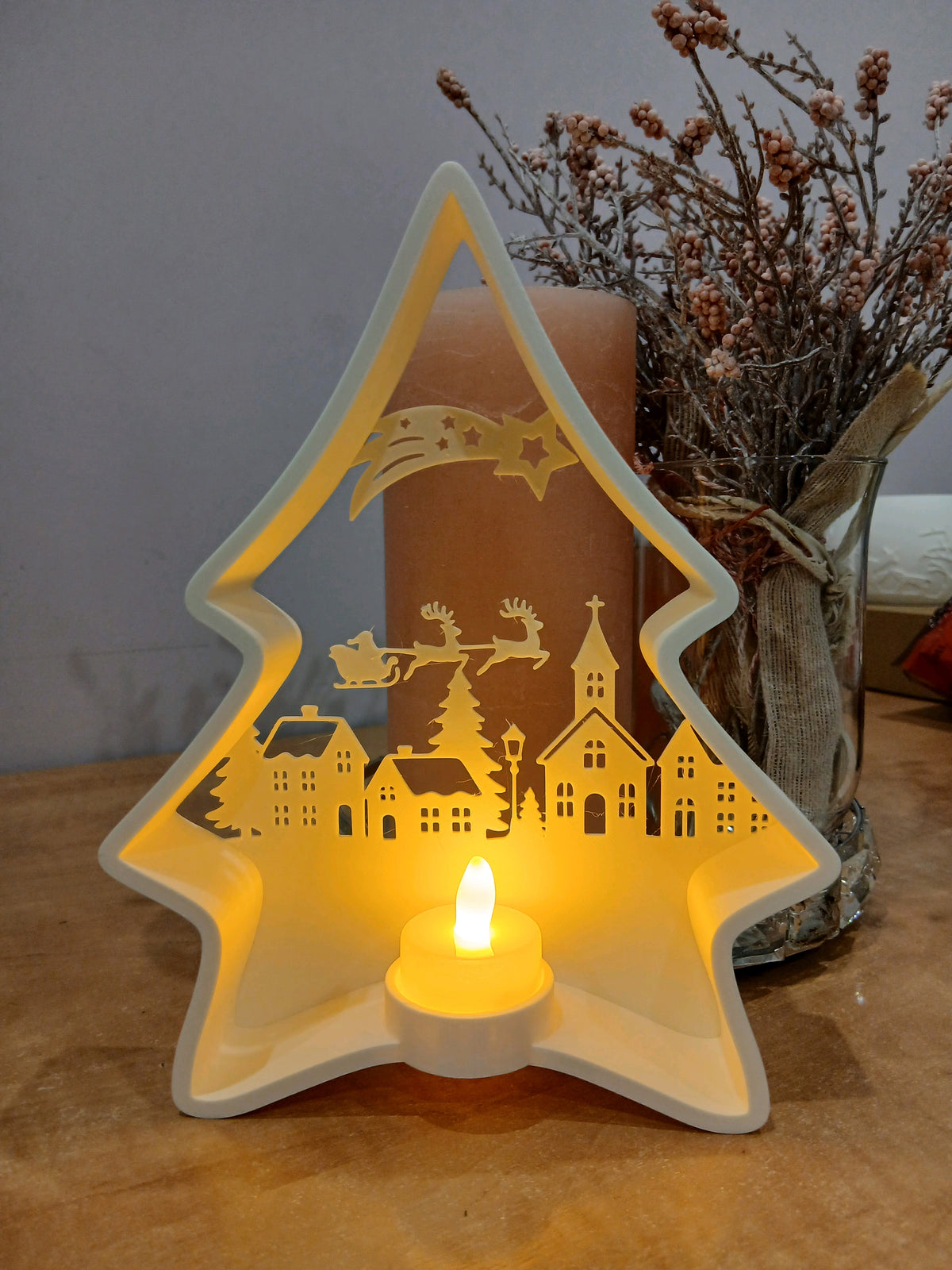 White tree-shaped tealight holder with a Christmas village, star and sleigh scene above the LED tealight cup