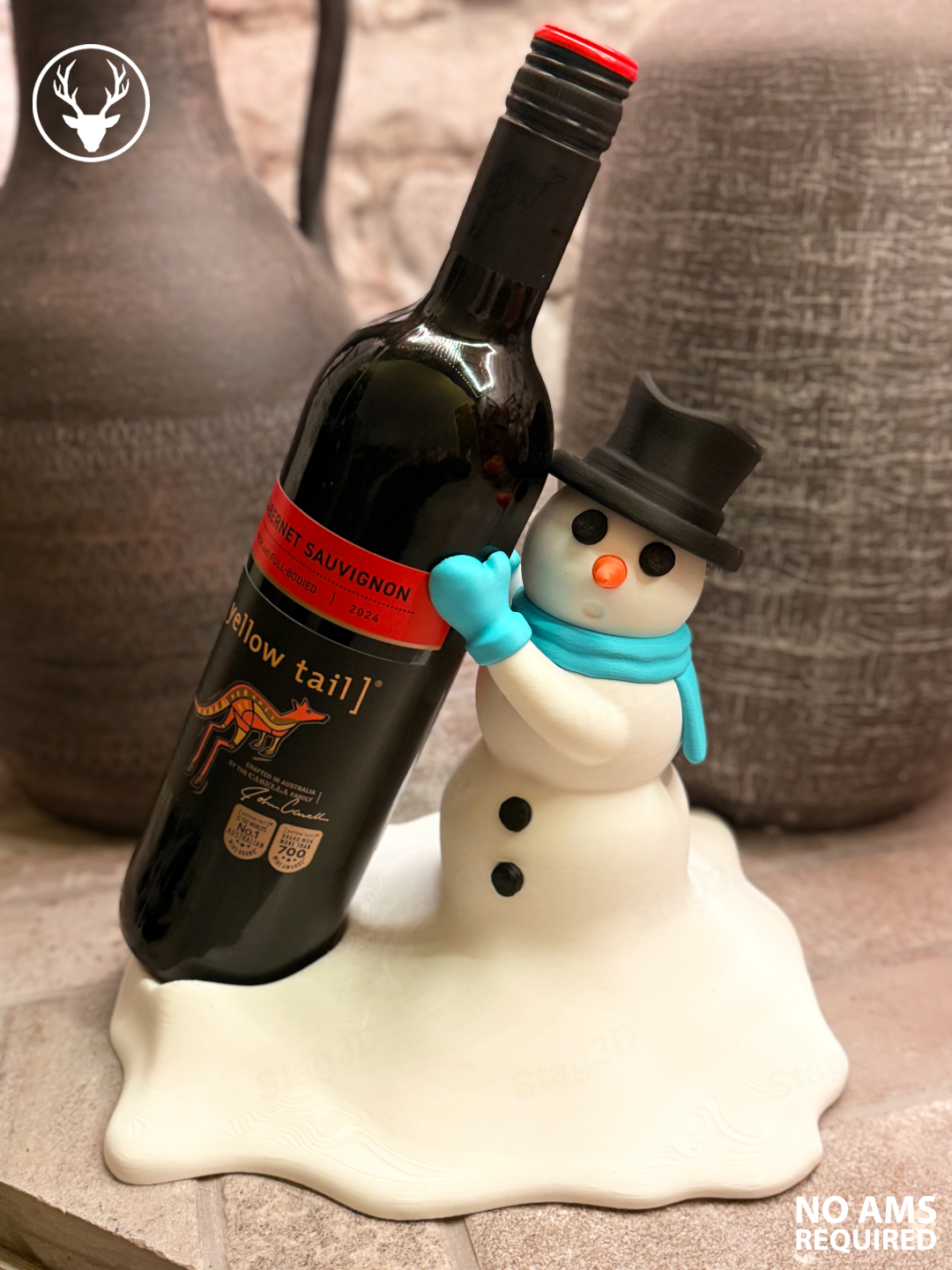 Snowman bottle holder with a white body and snowy base, black hat and buttons, orange nose and turquoise scarf beside a bottle