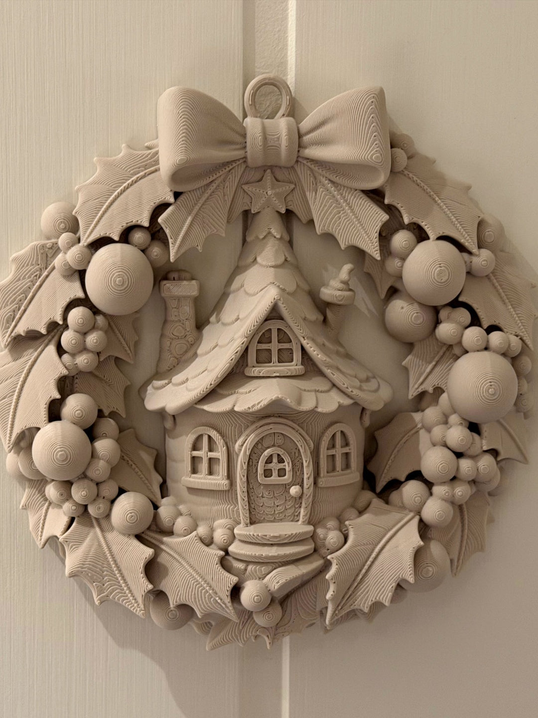 Fairy cottage Christmas wreath with a large bow, sculpted leaves and berries, shown hanging on a pale wall