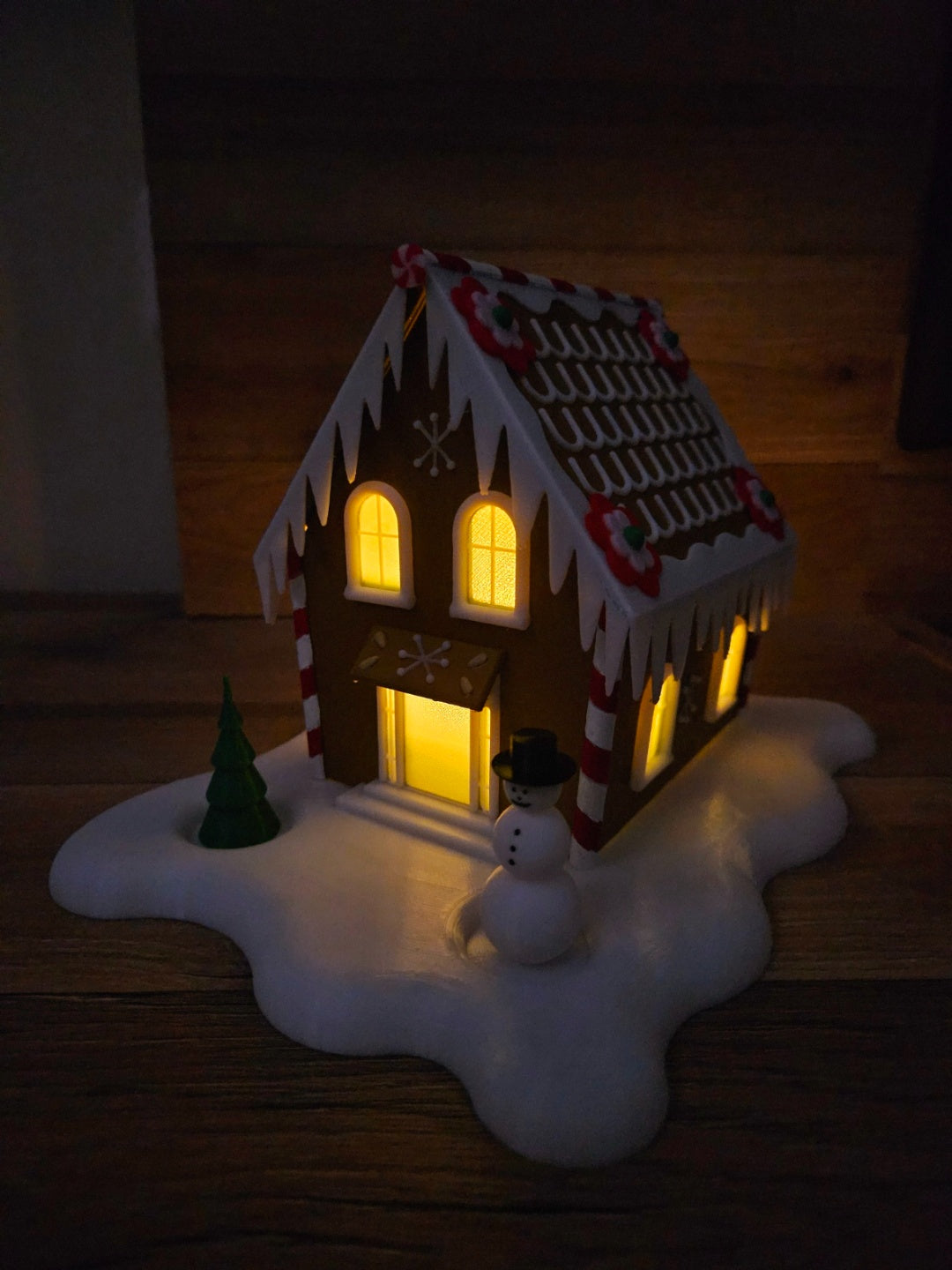 Festive gingerbread-style cabin with warm glowing windows, snowy base and snowman