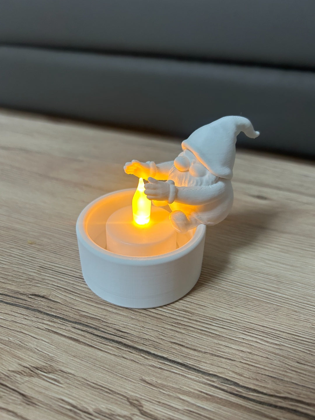 White Santa gnome leaning over the open cup of a tealight holder with a glowing LED light