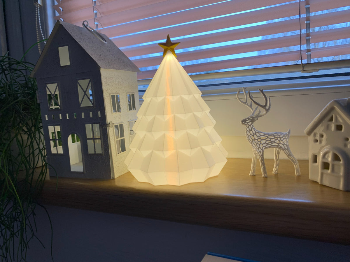 White geometric Christmas tree tealight holder with gold star topper displayed with winter village decor