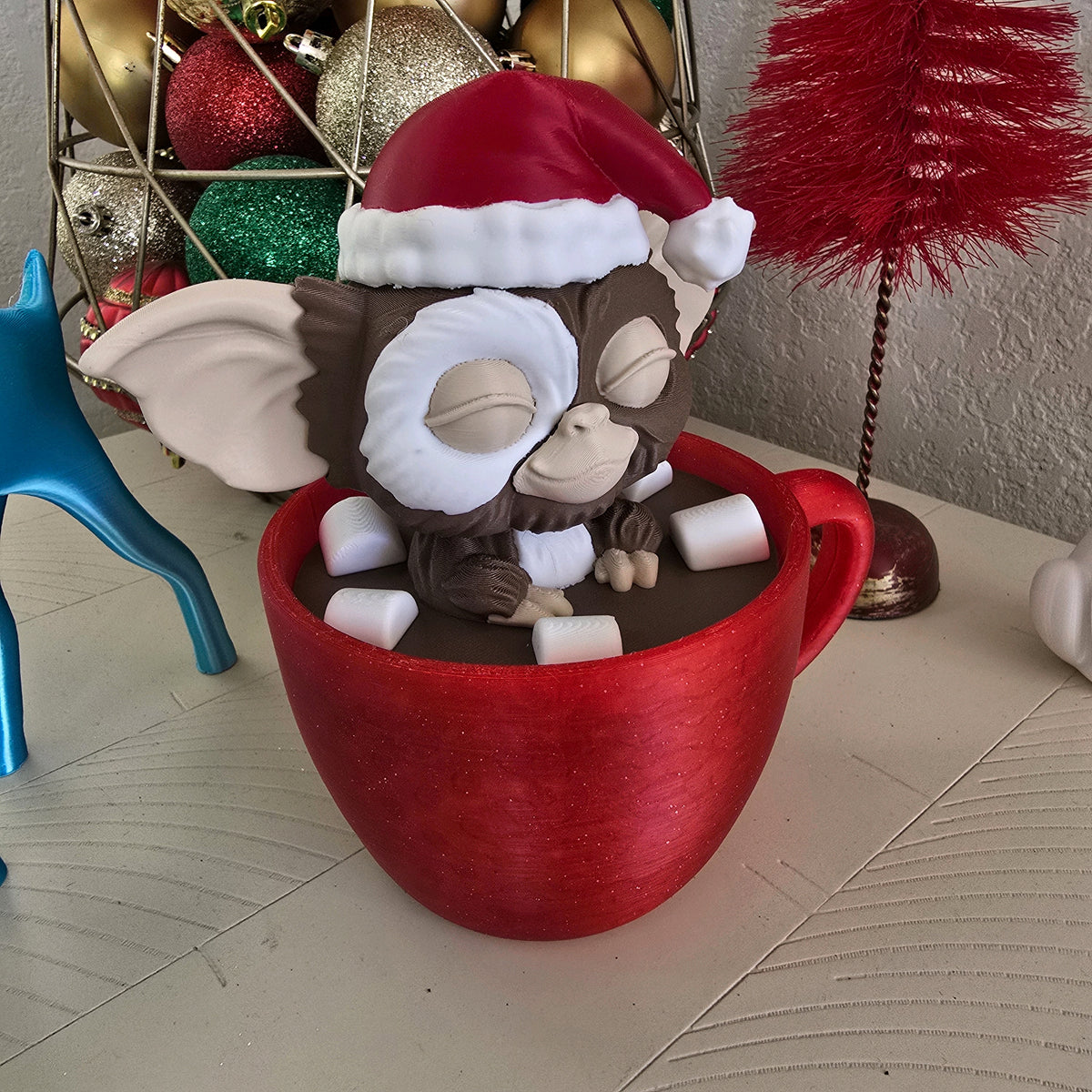 Gizmo in a red mug ornament displayed with Christmas baubles