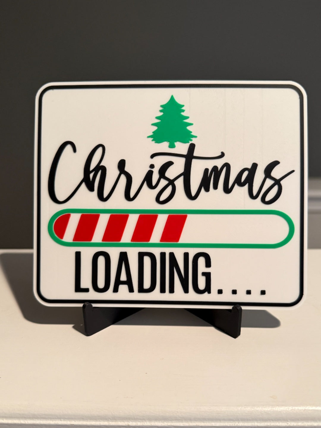 Freestanding cream Christmas Loading sign with a green tree, red-and-cream progress bar, black lettering and black easel stand