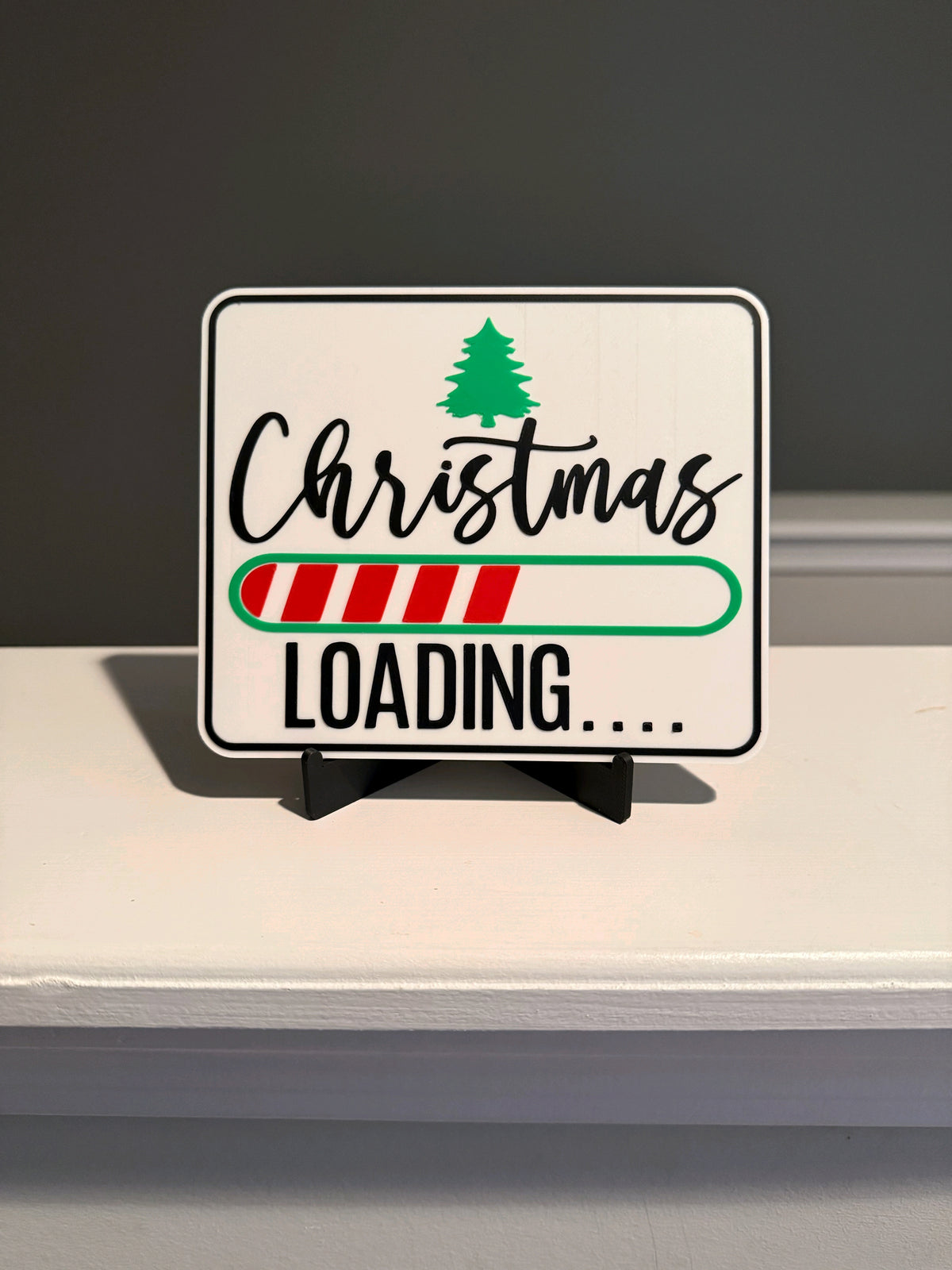 Christmas Loading Sign standing on its black easel on a pale shelf