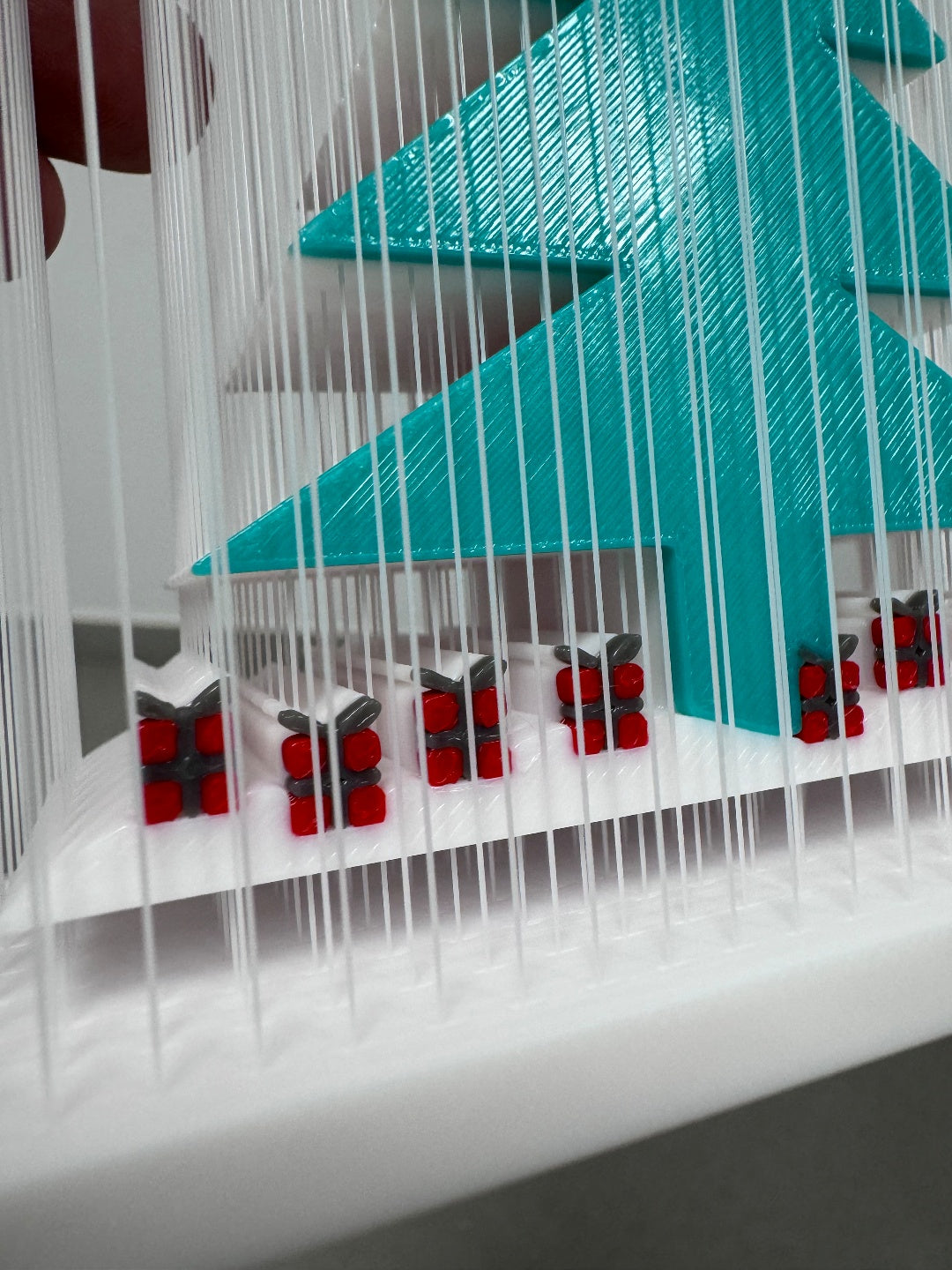 Closer view of the teal-green tree and the small red-and-dark decorative accents along the base inside the white strand frame.
