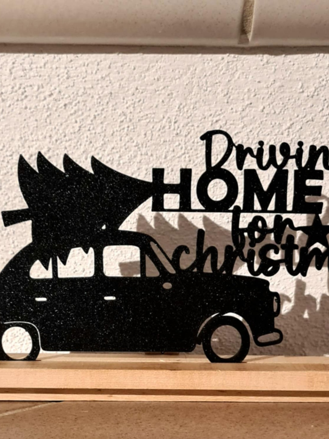 Close-up of a black cut-out car carrying a Christmas tree with Driving Home for Christmas wording on a natural wood base