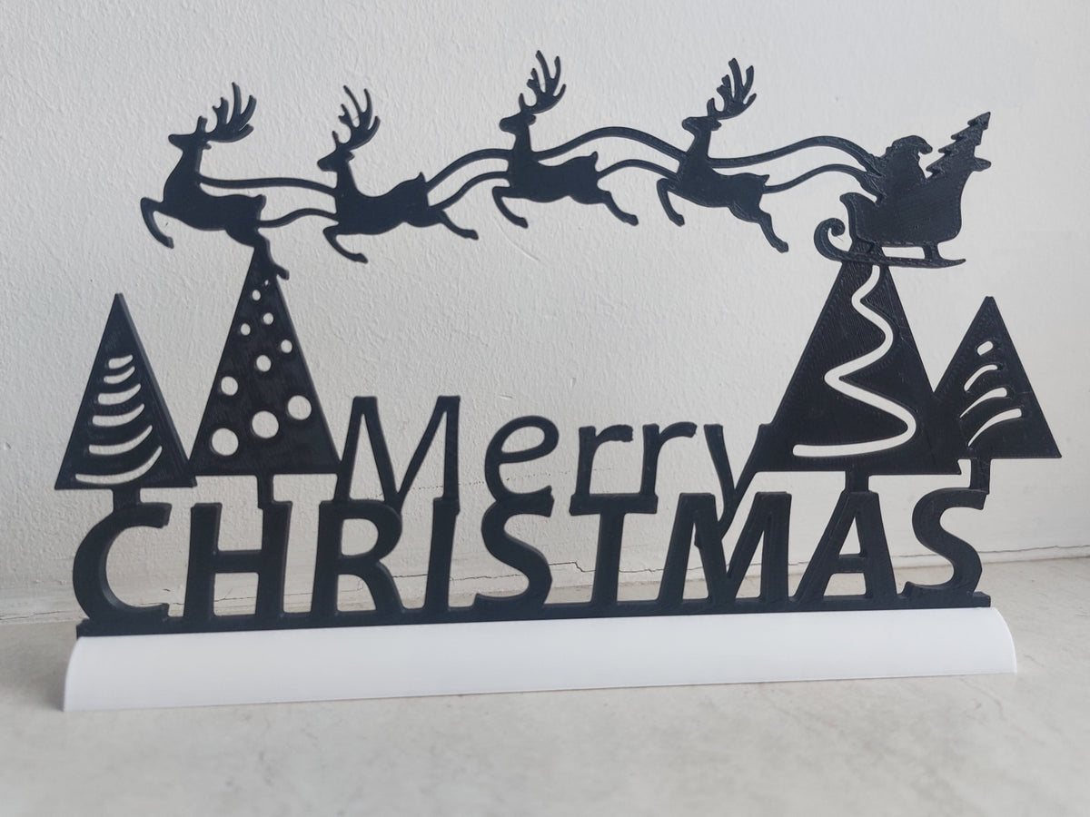 Freestanding black Merry Christmas sign on its white base, with festive trees and a sleigh scene