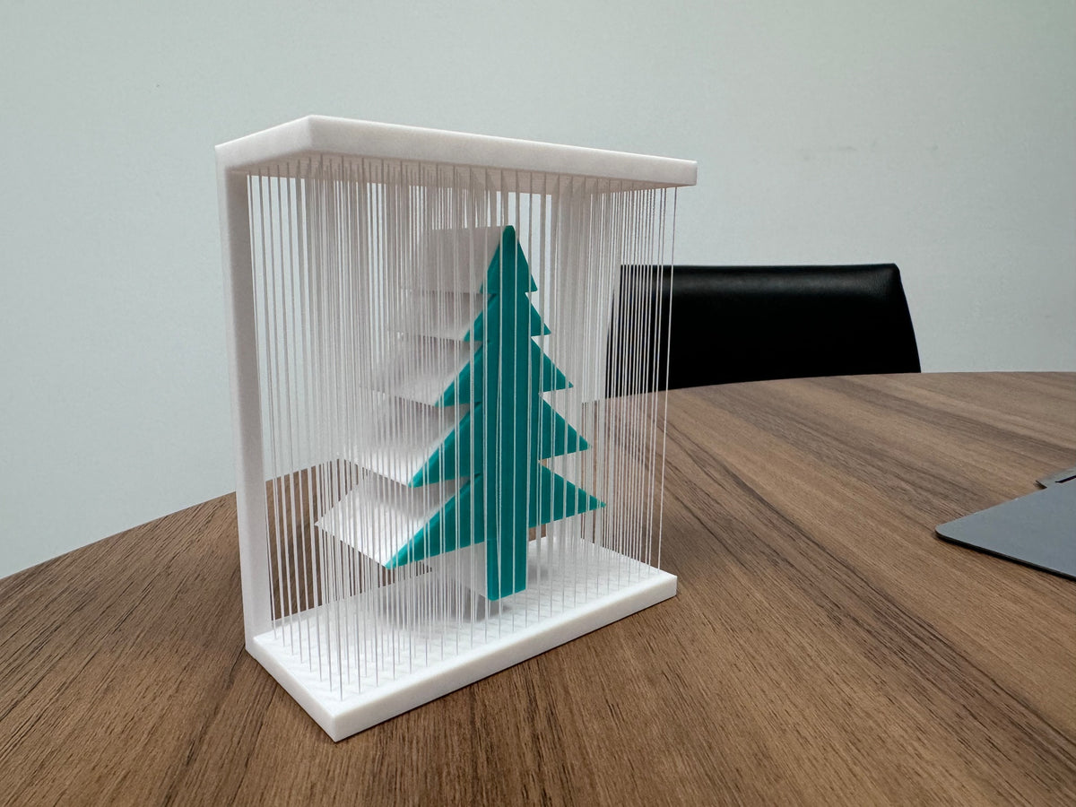 Second angle of the teal-green tree suspended inside a white frame of fine vertical strands.