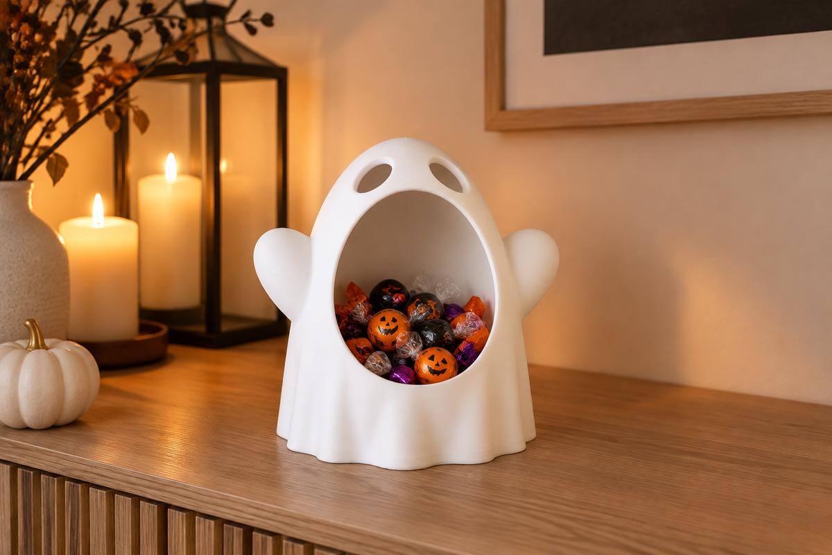 White wide-mouthed ghost sweet bowl holding wrapped Halloween candy on a candlelit console