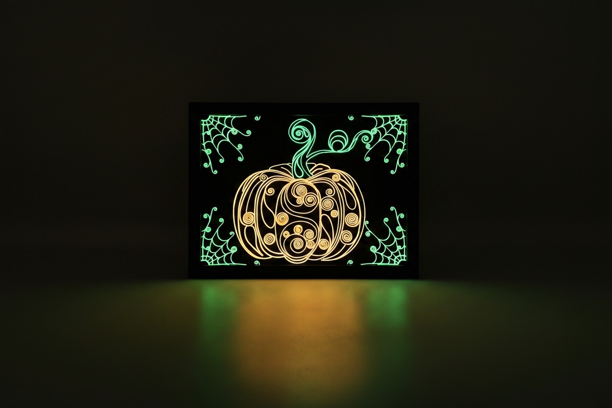 Spooky Swirls Glow-in-the-Dark Pumpkin shadow box in a dark room glowing warm golden-yellow pumpkin with vivid green stem and spiderweb corners casting a warm pool of light beneath