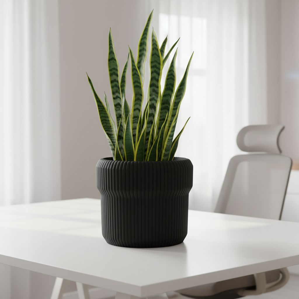 Matte black Venlo ribbed planter with a snake plant on a minimalist white desk