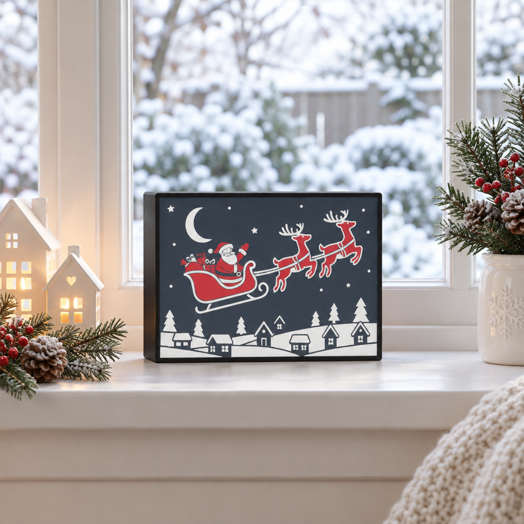 Black-framed Santa on Sleigh picture displayed on a snowy windowsill