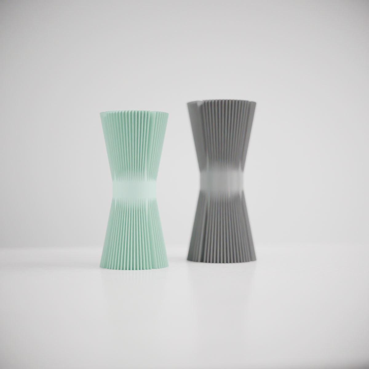 Ripple Twist Vase slim hourglass profile tight vertical ribbed ripple texture mint green and charcoal grey pair close up on white surface white background showing dramatic waist pinch and rib detail