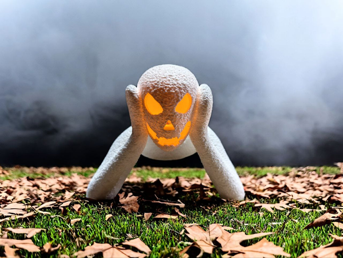 White crawling ghost lamp with glowing orange face displayed among autumn leaves