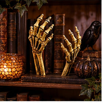 Gold-tone skeletal hands emerging from a flower bed arranged with pumpkins