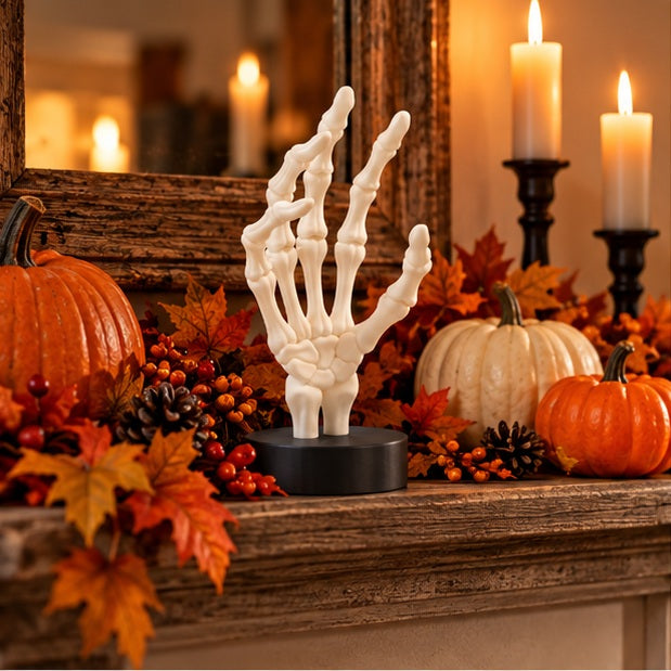 White skeletal hand on a black display base among autumn leaves and pumpkins