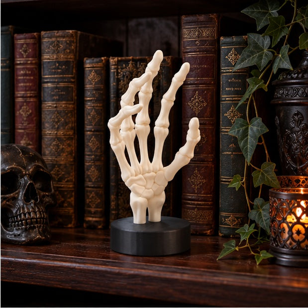 White skeletal hand displayed on a dark bookshelf beside old books and gothic décor