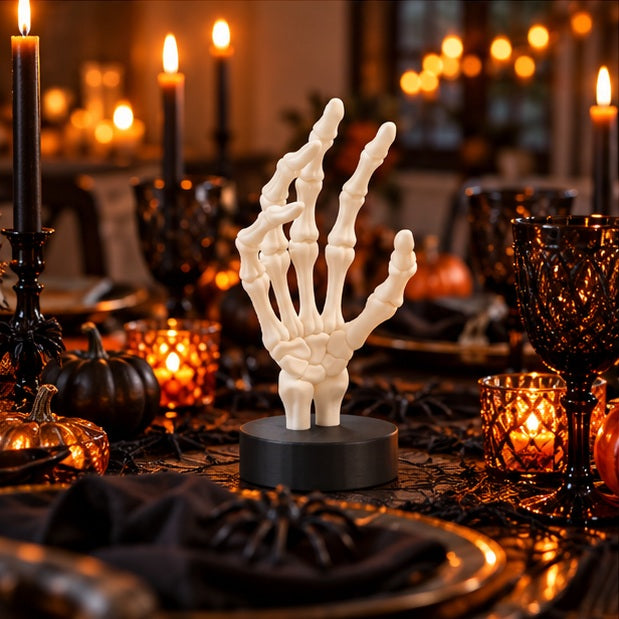 White skeletal hand on a black base in an autumn Halloween arrangement with pumpkins