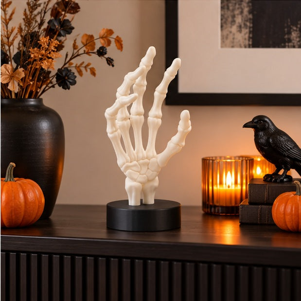 White skeletal hand displayed by candlelight with dark books and gothic accents