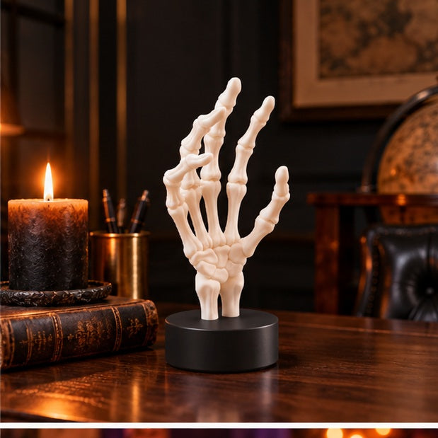 White skeletal hand displayed with a raven ornament, pumpkins and candlelight