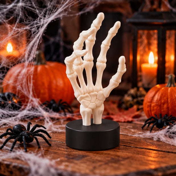 White skeletal hand beside a candle and dark books in a spooky interior