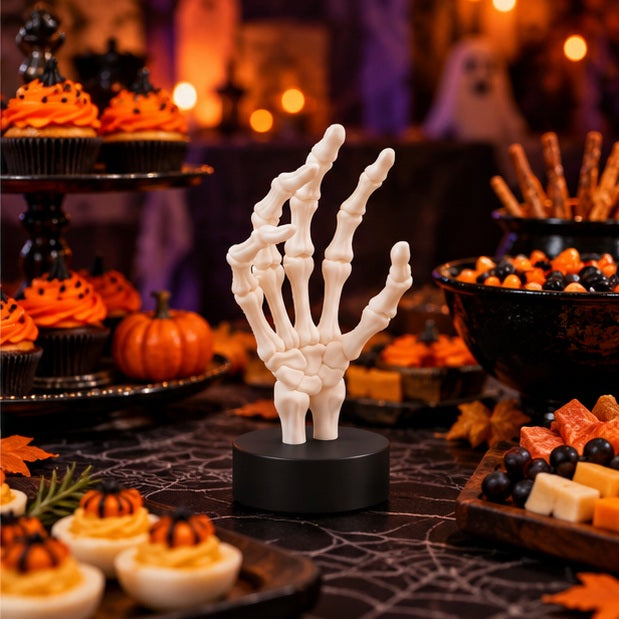 White skeletal hand featured in a Halloween party scene with pumpkins and treats